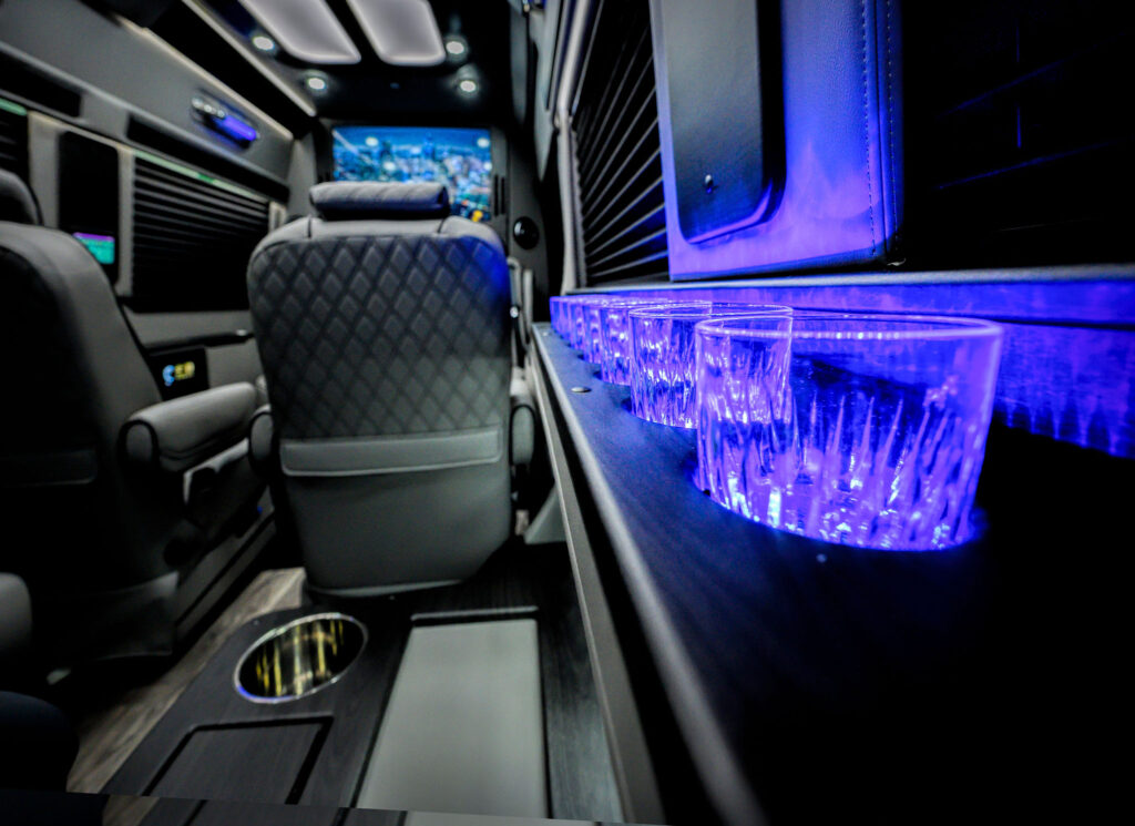 Interior photo of the Elite Transportation Cincinnati Mercedes-Benz Sprinter Limo Van featuring cups illuminated blue and an HDTV in front of leather chairs